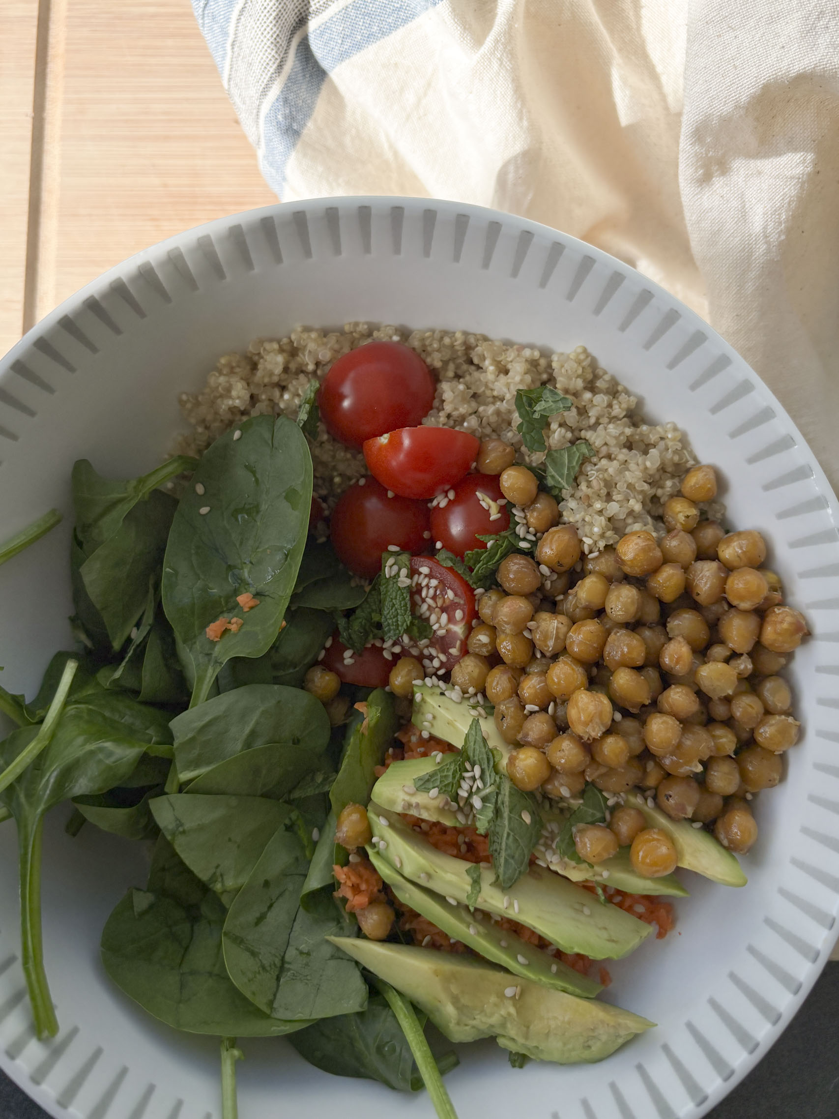 Zutaten für die Quinoa-Bowl: Quinoa, Kichererbsen, Kirschtomaten, Möhre, Avocado und Minze auf einer natürlichen Küchenoberfläche arrangiert